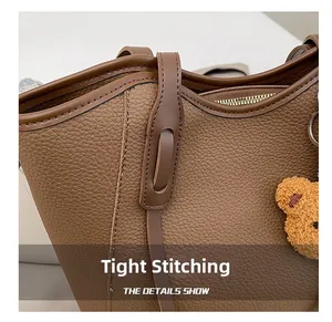 Detailed close-up of brown litchi grain leather bag with golden zipper and plush bear charm