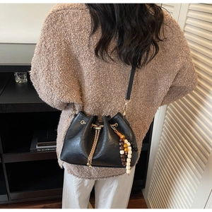 Detail of black leather bucket bag with gold hardware and colorful wooden bead tassel