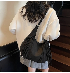 Detailed view of black suede hobo bag with long tassels on a model in a casual setting