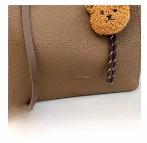 Detail of brown litchi pattern leather tote bag with gold logo and plush bear charm