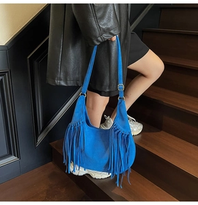 Detail of vibrant blue suede shoulder bag with long fringes against dark stairs