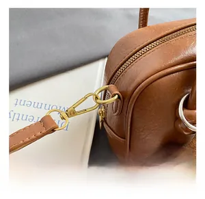 Détail d'un sac en cuir marron montrant le crochet doré et le charm en bois
