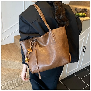 Dettaglio di una borsa tote in ecopelle marrone con ciondolo decorativo di nappe in legno