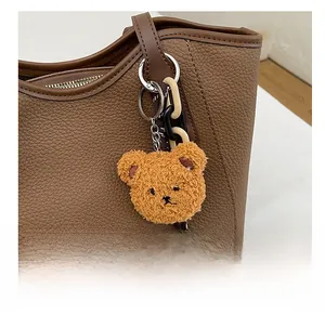 Close-up of a brown plush bear charm attached to a brown lychee pattern leather tote bag