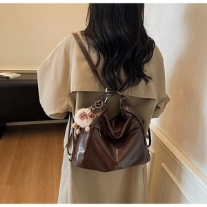 Detail of dark brown leather tote bag with plush charm on a model in beige coat