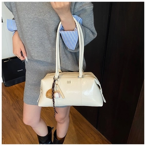 Detail of cream white patent leather Boston bag featuring a sporty baseball charm accessory