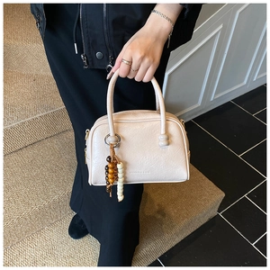 Detail of beige lychee pattern leather handbag with artistic beaded charm and embossed text
