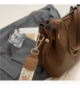 Détail du sac seau en cuir marron avec une large bandoulière brodée aux motifs géométriques
