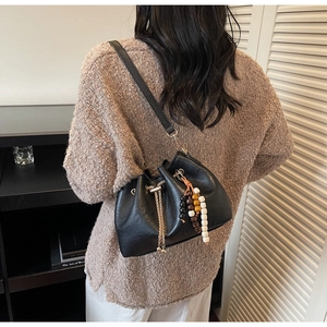 Detail of black leather drawstring bucket bag with colorful beads worn with a sweater