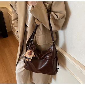Detail of dark brown leather shoulder bag with cute lion plush keychain and logo