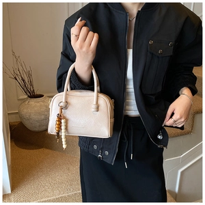 Détail du sac à main beige en cuir avec breloque en perles de bois sur veste noire