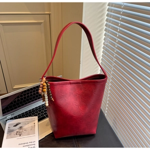 Detail of red vintage textured leather bucket bag with decorative wooden bead charm