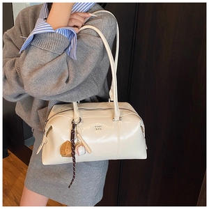 Macro detail of cream leather Boston bag featuring baseball charms and metal zipper finish