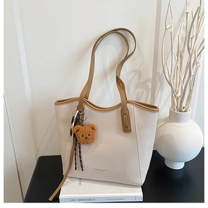 Detail of beige tote bag showing pebble leather texture and a cute brown bear charm