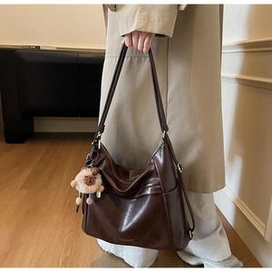 Fashionable dark brown leather tote bag with plush charm shown in a lifestyle outfit