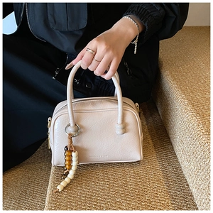 Detail of beige bowling bag with natural texture, round handles and beaded ornament