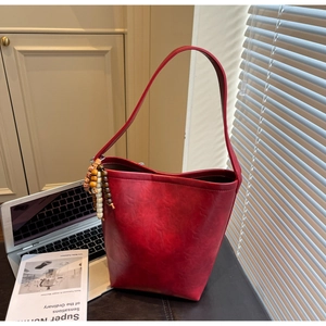 Detail of red bucket bag with wooden bead charm and faux leather texture on minimalist background