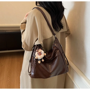 Detail of dark brown leather tote bag with drawstring side and cute plush charm