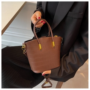 Detail of a brown crocodile pattern leather handbag with gold hardware and shoulder strap