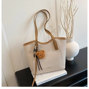 Detail view of beige lychee texture tote bag with brown straps and cute bear charm decor