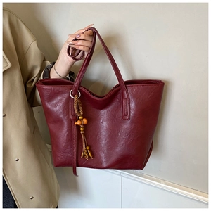 Dettaglio della borsa tote rosso scuro in finta pelle con ciondolo vintage in legno
