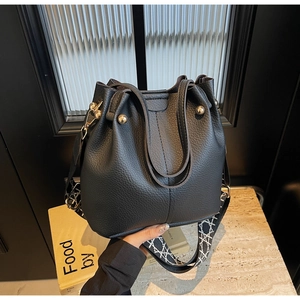 Détail du sac seau noir en cuir grainé avec bandoulière géométrique et boucles dorées