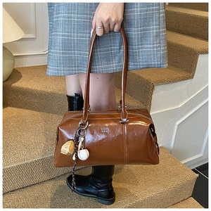 Close-up of dark brown glossy leather Boston bag with a baseball charm and metal logo