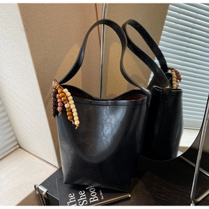 Detail of a black leather bucket bag with a trendy brown beaded tassel accessory