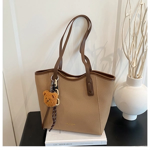 Detail of brown lychee grain leather tote bag with gold logo and plush bear charm