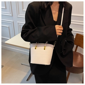 Detail view of white crocodile texture mini bucket bag with gold accents on a black blazer
