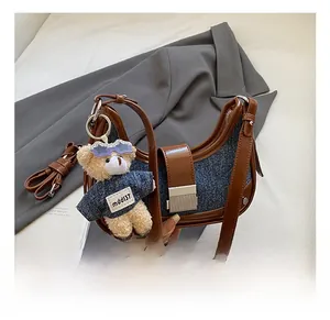 Detail of blue denim crescent bag with brown leather trim and a cute teddy bear charm