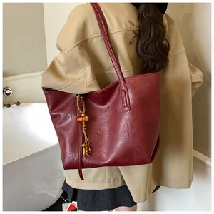 Dettaglio borsa tote bordeaux in pelle con nappina in legno e tracolla singola