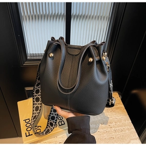 Détail du sac seau noir en cuir grainé avec une large bandoulière à motifs variés