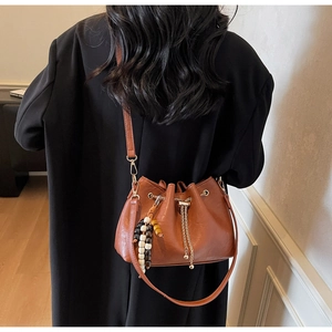 Detail of brown leather bucket bag with drawstring, beaded charm and gold chain fringe