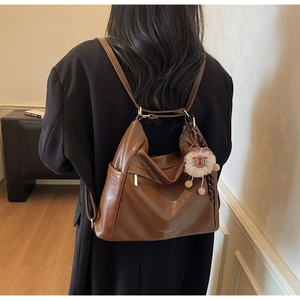 Detail of dark brown leather tote bag with gold logo and plush lion charm on model
