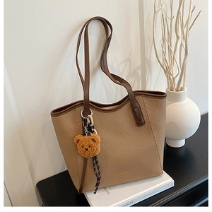 Close-up of khaki lychee leather tote bag with brown plush bear charm on white book