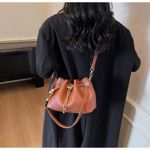 Detail view of brown leather bucket bag with gold chain and beaded charm on black coat