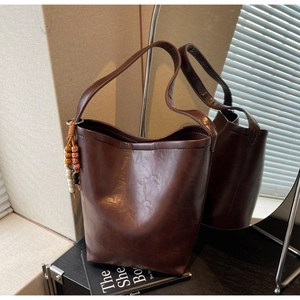 Detail of dark brown leather bucket bag featuring decorative multi-color beaded tassel charm