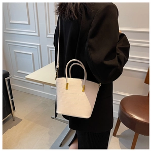 Detail of white crocodile pattern bucket bag with golden hardware and adjustable strap
