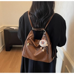 Detail of a brown leather shoulder bag with a cute plush sheep charm and logo text