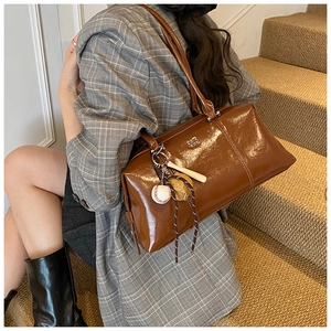 Detail view of brown glossy leather Boston bag with baseball charm and brand logo