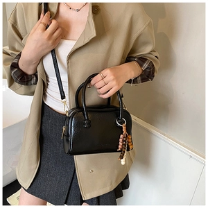 Close-up of black bowling handbag styled with a khaki blazer and pleated skirt.
