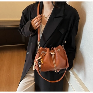 Detail of brown pleated bucket bag with gold chains and colorful bead tassel pendant