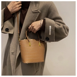 Detail of light brown crocodile textured bucket bag with gold hardware and strap
