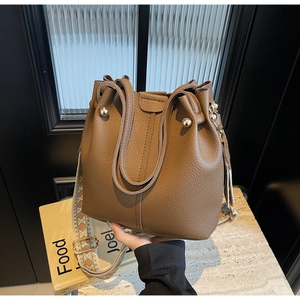 Gros plan sur un sac seau marron en cuir grainé avec une large bandoulière brodée
