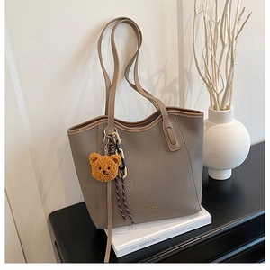 Detail of grey pebbled leather tote bag with yellow bear charm on a stack of books