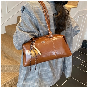 Detail of a brown glossy leather shoulder bag with a sporty baseball-themed charm