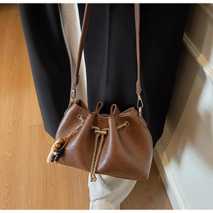 Detail of a brown leather bucket bag featuring drawstring closure and gold chain accent