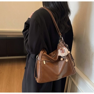 Detail of dark brown leather tote bag with gold brand stamp and plush pendant