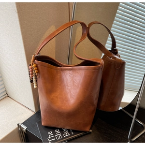 Detail of caramel brown bucket bag with wide shoulder strap and colorful wooden bead charm